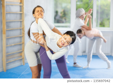 Woman and girl in gym perform basic elements of krav maga self-defense system. 135697042