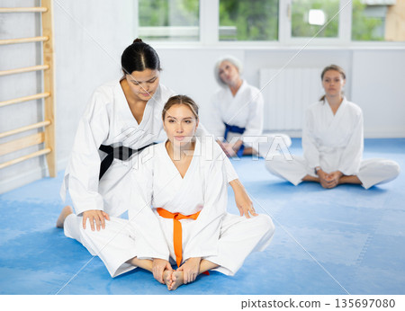 Girl before training martial arts performs stretching butterfly with couch help to warm up muscles. Girl before training martial arts performs stretching butterfly with couch help to warm up muscles. 135697080