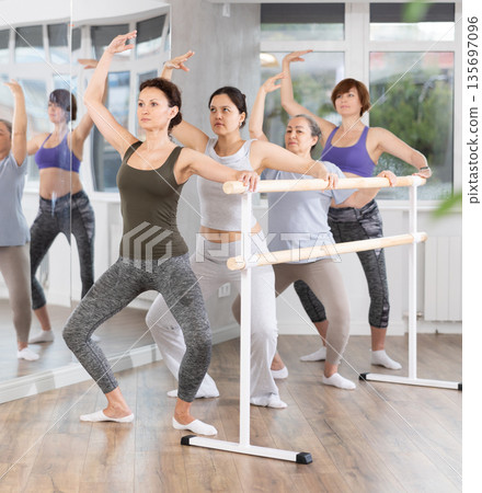 Group of female beginners performing plie at barre 135697096