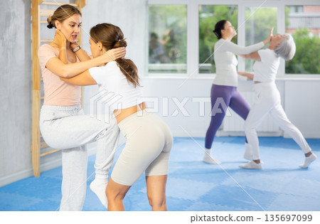 Woman practices blows to head of her attacking woman during self defense training 135697099