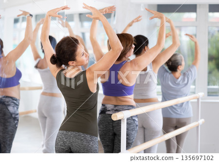 Group of women stand in fifth position at barre 135697102