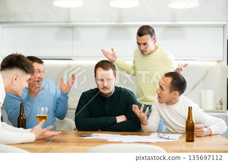 Male friends read a financial or legal document, drink beer and try to solve financial problems by consulting each other while sitting at table Male friends read a financial or legal document, drink beer and try to solve financial problems by consulting each other while sitting at table 135697112