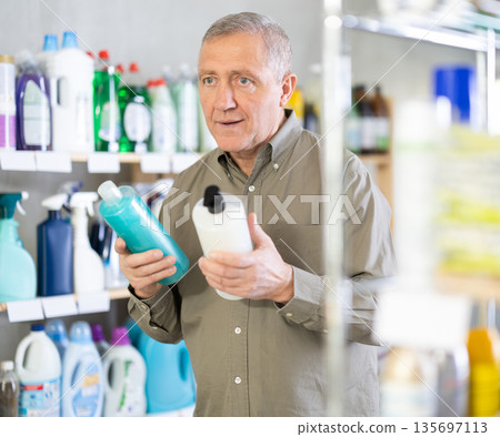 Male buyer chooses shampoo or shower gel in household goods department of supermarket Male buyer chooses shampoo or shower gel in household goods department of supermarket 135697113