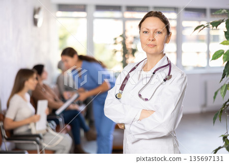 Smiling female doctor standing with crossed arms in lobby of clinic 135697131