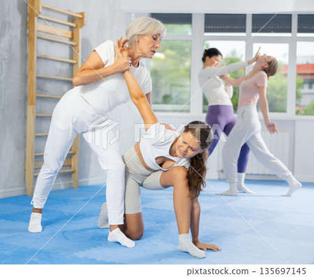 Mature woman applying arm lock technique in mock bout during self-defense class 135697145
