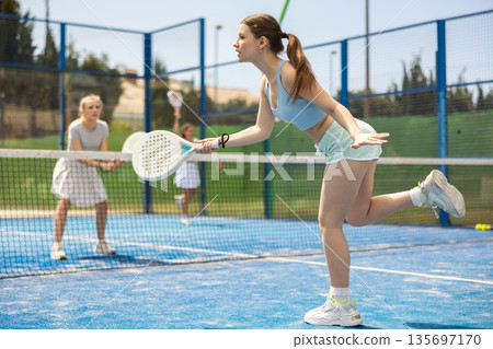Young woman playing paddle tennis against team of women 135697170