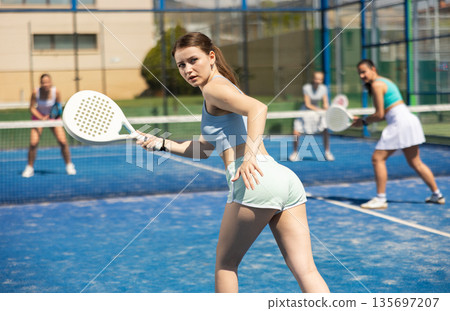 Young woman playing paddle tennis against team of women 135697207