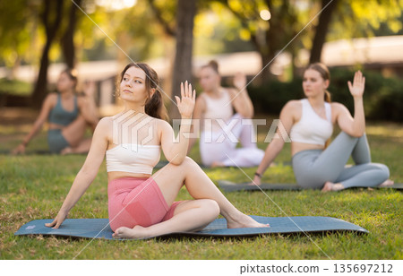 Yoga lesson visitors girls perform lord of fishes in park Yoga lesson visitors girls perform lord of fishes in park 135697212