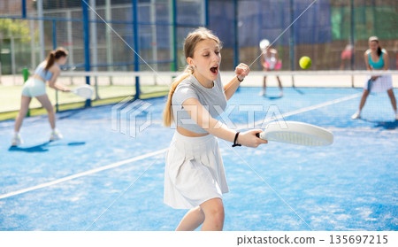 Young woman playing paddle tennis against team of women 135697215