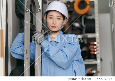 Female worker carrying a stepladder Female worker carrying a stepladder 135697247