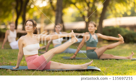 Yoga lesson visitors girls perform eka padahastasana salamba navasana in park 135697255