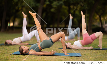 Yoga lesson visitors girls perform Setu Badha Sarvangasana in park Yoga lesson visitors girls perform Setu Badha Sarvangasana in park 135697258