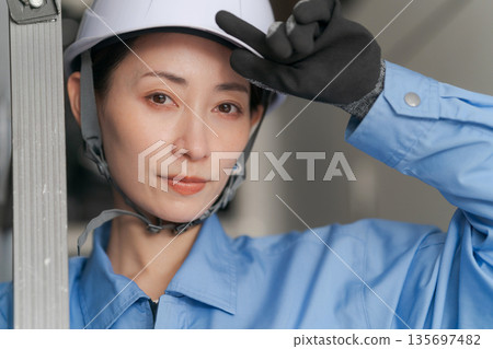 Smiling female worker carrying a stepladder 135697482