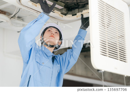 A female worker inspecting an air conditioner 135697706