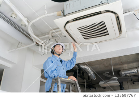 A female worker inspecting an air conditioner 135697767