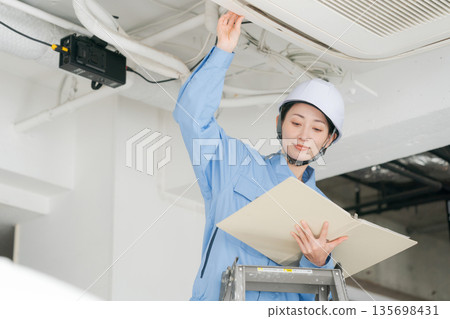 A female worker inspecting an air conditioner A female worker inspecting an air conditioner 135698431