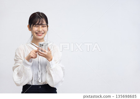 A smiling young woman operating a smartphone in front of a white background 135698685