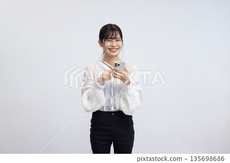A smiling young woman operating a smartphone in front of a white background 135698686