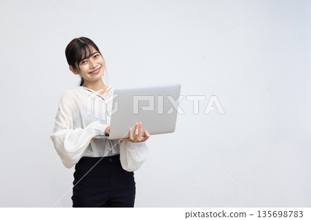 A young woman smiling while using a laptop in front of a white background 135698783