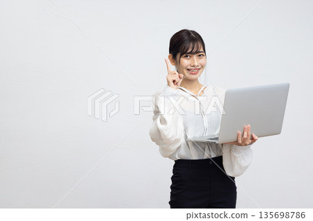 A young woman holding a laptop and pointing her index finger up in front of a white background A young woman holding a laptop and pointing her index finger up in front of a white background 135698786
