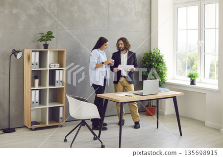 Two business people man and woman standing in office near the workplace and talking. Two business people man and woman standing in office near the workplace and talking. 135698915