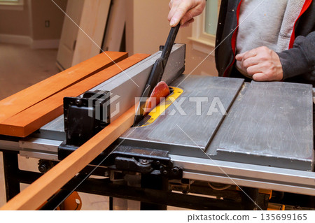 Carpenter is using table saw to cut long strip of wood in workshop. 135699165
