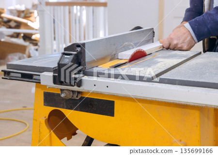 Carpenter operates table saw in construction area saw cuts through piece of wood. 135699166