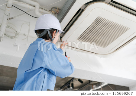 A female worker inspecting an air conditioner A female worker inspecting an air conditioner 135699267