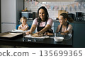 Young mother and her daughters work together at the kitchen table rolling ginger cookie dough, home baking concept 135699365