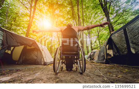 Disabled man resting in a campsite with friends. Wheelchair in the forest  135699521