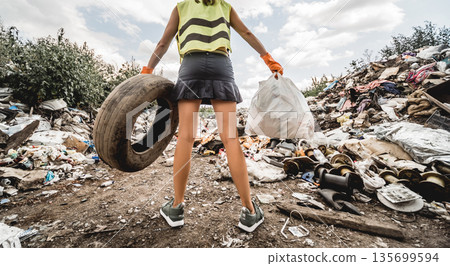 Woman volunteer helps clean the field of plastic garbage and old tires.  135699594