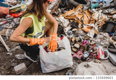 Woman volunteer helps clean the field of plastic garbage. Bushes and sky Woman volunteer helps clean the field of plastic garbage. Bushes and sky 135699601