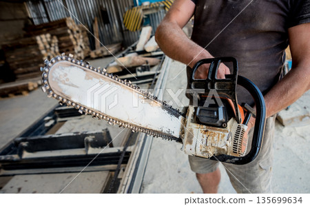 Woodcutter cutting tree with chainsaw on sawmill. Modern sawmill Woodcutter cutting tree with chainsaw on sawmill. Modern sawmill 135699634