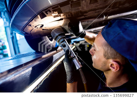 Car mechanic examining car suspension of lifted automobile at service station Car mechanic examining car suspension of lifted automobile at service station 135699827