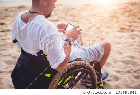 Disabled man in a wheelchair on the beach. Disabled man in a wheelchair on the beach. 135699841