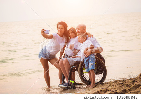 Disabled man in a wheelchair with his family on the beach. 135699845