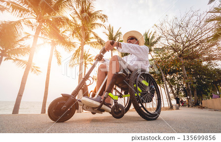 Disabled man in a wheelchair with electric scooter on the beach Disabled man in a wheelchair with electric scooter on the beach 135699856