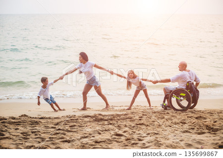 Disabled man in a wheelchair with his family on the beach. Disabled man in a wheelchair with his family on the beach. 135699867