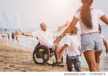 Disabled man in a wheelchair with his family on the beach. Disabled man in a wheelchair with his family on the beach. 135699874