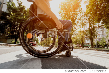 Handicapped man in wheelchair crossing street road Handicapped man in wheelchair crossing street road 135699934