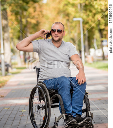 Handicapped man in wheelchair at the park alley use a smartphone Handicapped man in wheelchair at the park alley use a smartphone 135699936