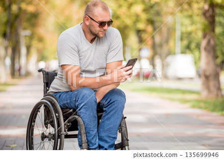Handicapped man in wheelchair at the park alley use a smartphone 135699946