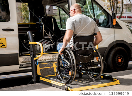 A man in a wheelchair on a lift of a vehicle for people with disabilities A man in a wheelchair on a lift of a vehicle for people with disabilities 135699949