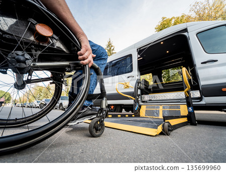 A man in a wheelchair moves to the lift of a specialized vehicle A man in a wheelchair moves to the lift of a specialized vehicle 135699960