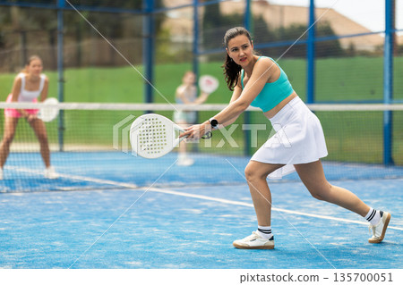 Adult woman plays paddle tennis against team of women 135700051