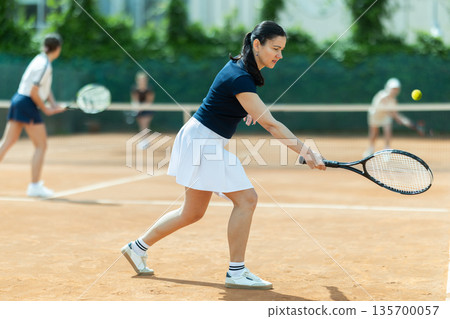Adult woman playing doubles tennis on court 135700057