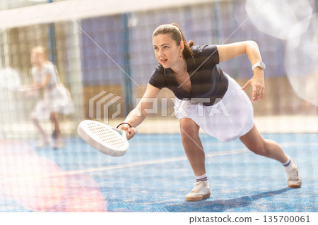 Adult woman playing doubles padel tennis Adult woman playing doubles padel tennis 135700061