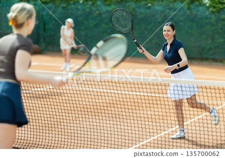 Adult woman playing doubles tennis on court Adult woman playing doubles tennis on court 135700062