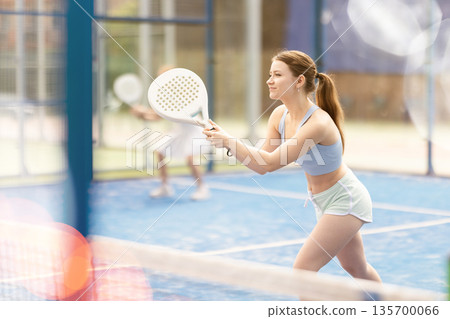 Woman with racket on court playing paddle in the background of sunshine Woman with racket on court playing paddle in the background of sunshine 135700066