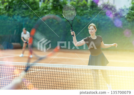 Young woman playing doubles tennis on court 135700079